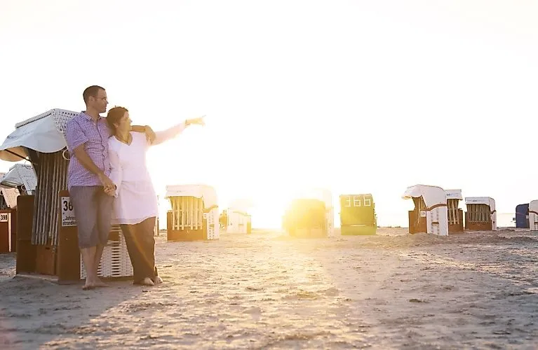 Paar steht barfuß am Norddeicher Strand vor Sonnenuntergang zwischen Strandkörben.