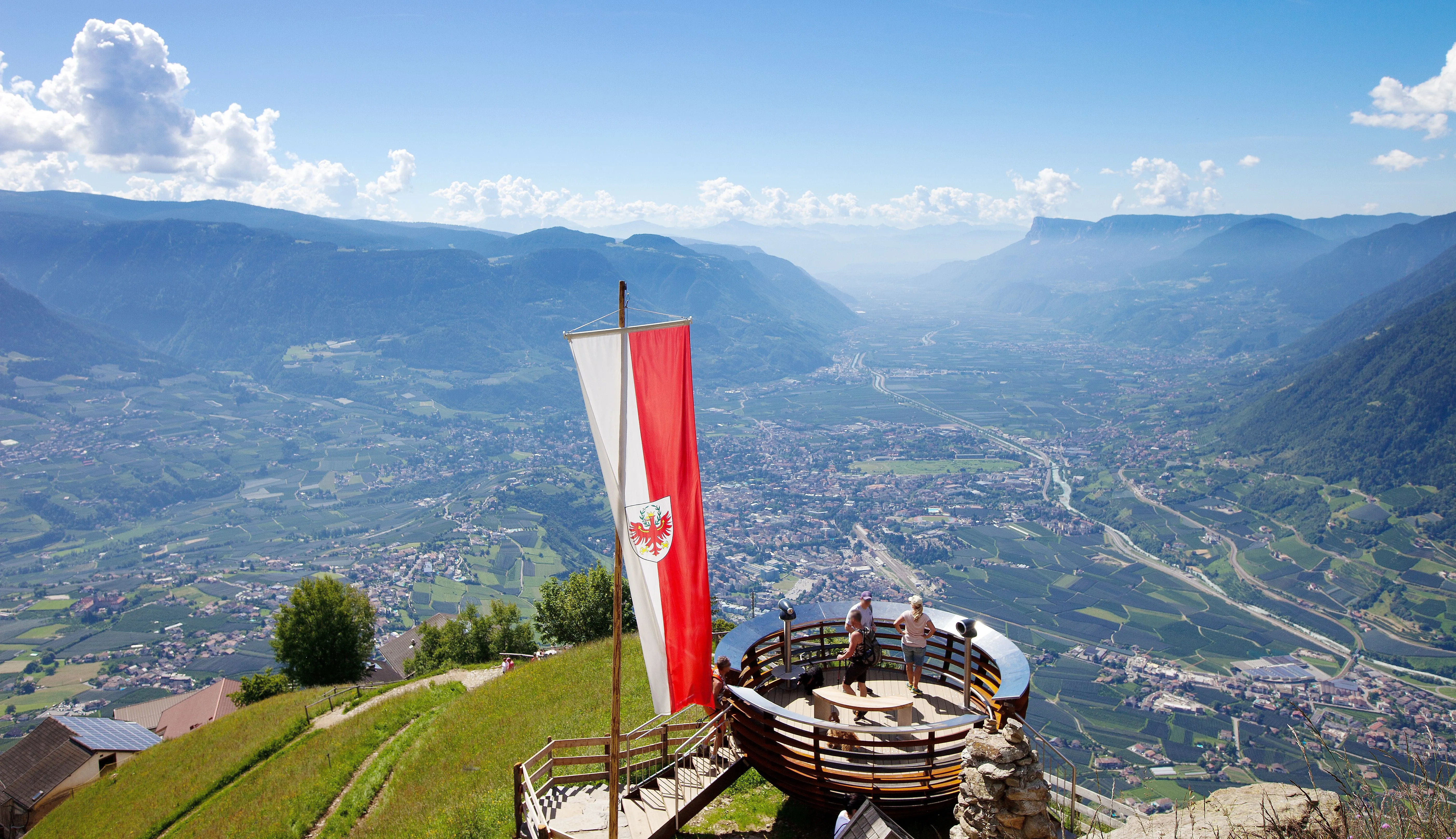 Atemberaubendes Panorama über Meran und das Etschtal von einem Aussichtspunkt mit Südtiroler Flagge.