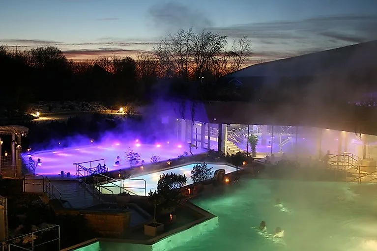 Stimmungsvoll beleuchtete Außenbecken der PanoramaTherme Beuren bei Nacht mit aufsteigendem Dampf