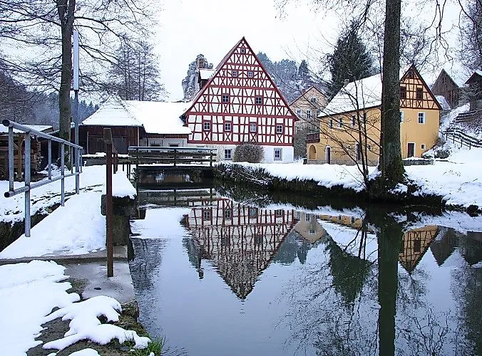 Half-timbered houses in winter in Tüchersfeld near Pottenstein with reflection in the water