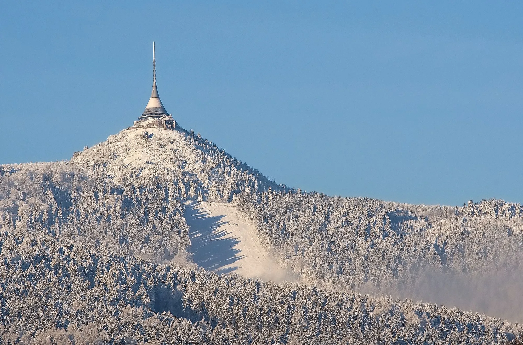 Schneebedeckter Berg Ještěd mit Fernsehturm und Hotel auf dem Gipfel bei blauem Himmel.