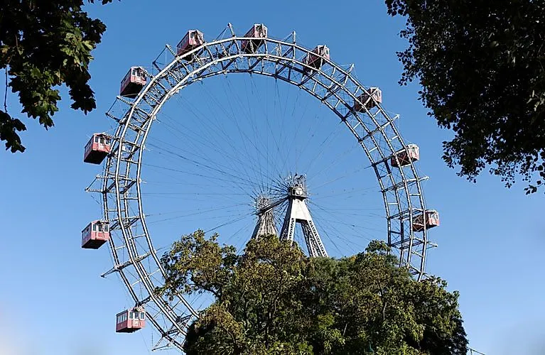 Wiener Riesenrad im Prater bei blauem Himmel, umgeben von Bäumen – Wahrzeichen und beliebte Attraktion der Stadt