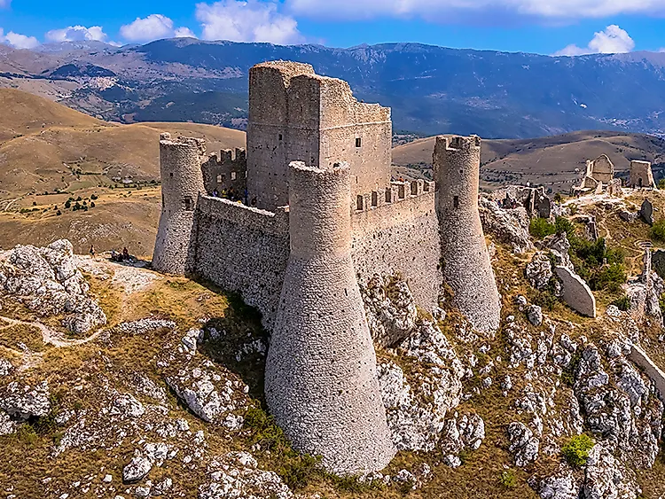 Mittelalterliche Burg auf einem Bergkamm in einer alpinen Landschaft mit Felsen und weiten Hügeln unter blauem Himmel
