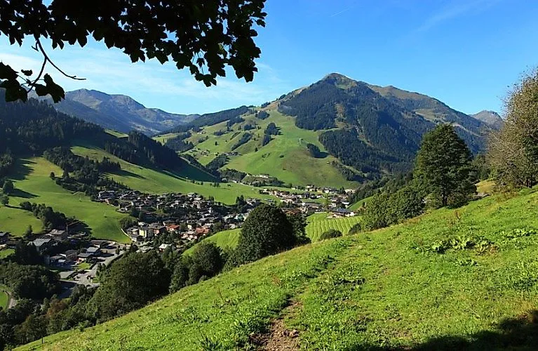 Panorama estivo di Saalbach con vista sullo Zwölferkogel e sui verdi prati alpini sotto un cielo azzurro.