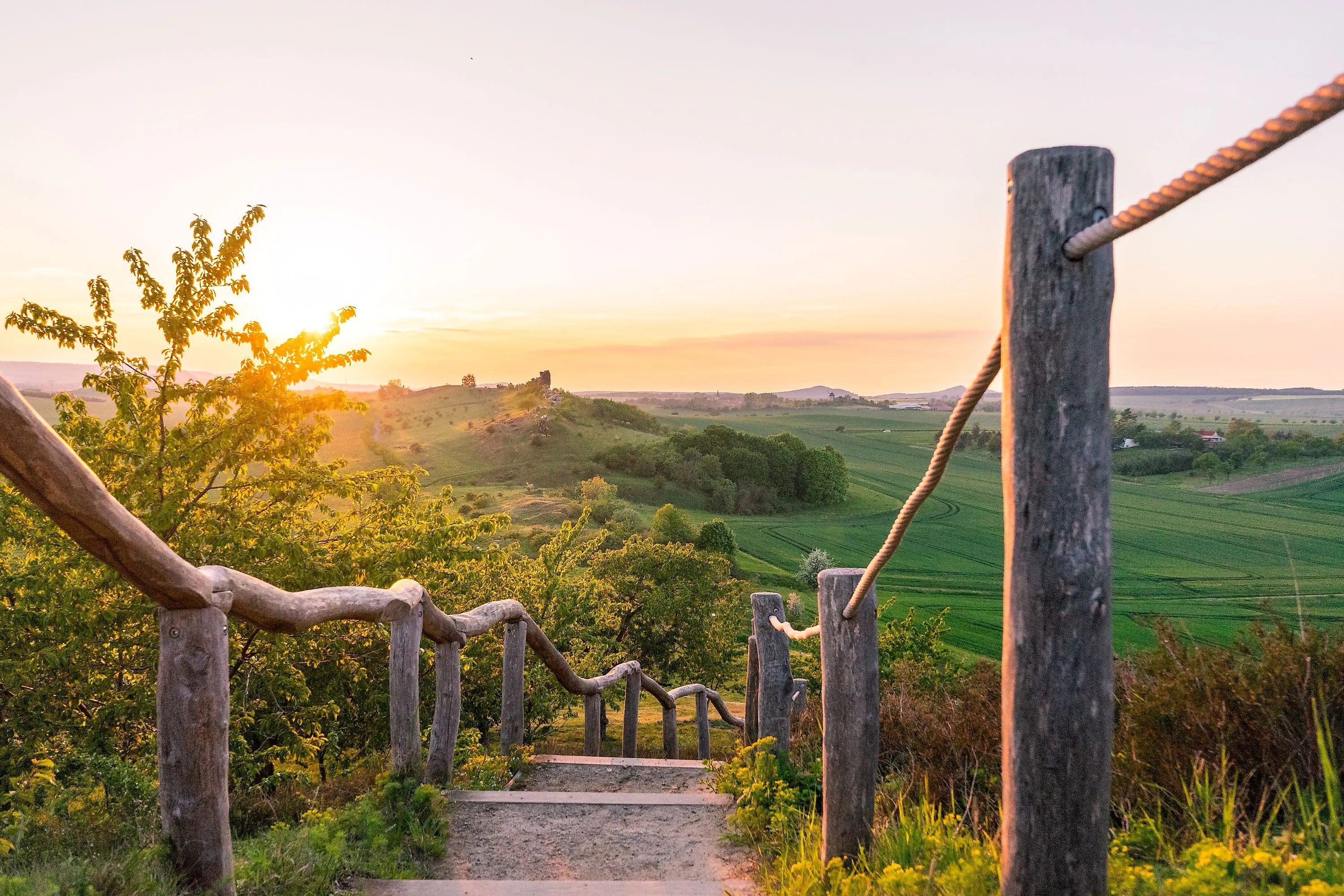 Wanderweg mit Holzgeländer bei Weddersleben mit Blick auf grüne Felder bei Sonnenuntergang