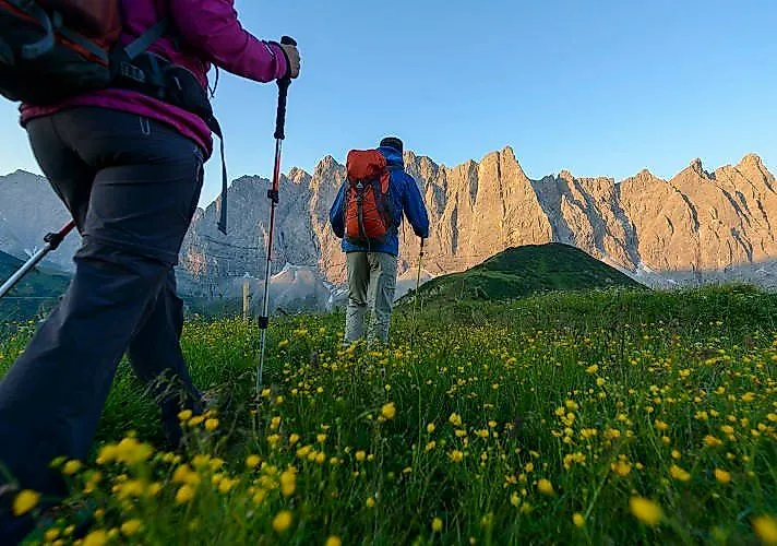 Escursionisti alle prime ore del mattino su un prato fiorito con vista sulle imponenti montagne del Karwendel vicino a Schwaz.