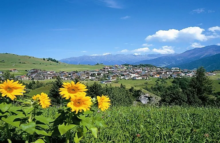 Blick auf das sonnige Serfaus mit blühenden Wiesen und Bergen im Sommer.