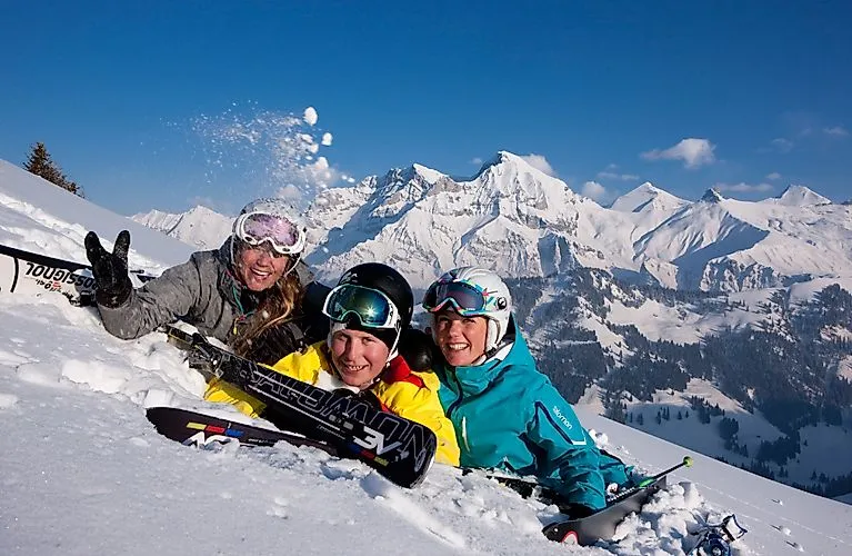 Drei Skifahrerinnen lachen im Schnee mit verschneiten Bergen im Hintergrund bei Adelboden