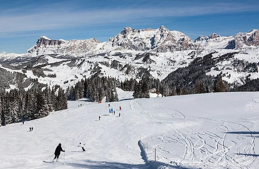 Skiërs op een besneeuwde piste met de majestueuze Dolomieten op de achtergrond bij Corvara.