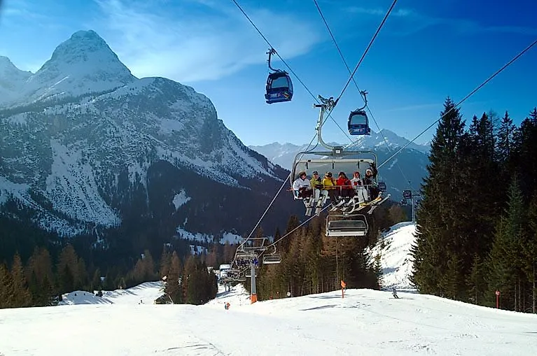 Ľudia na sedačkovej lanovke v Ehrwalde s výhľadom na zasneženú Zugspitze a okolité hory.