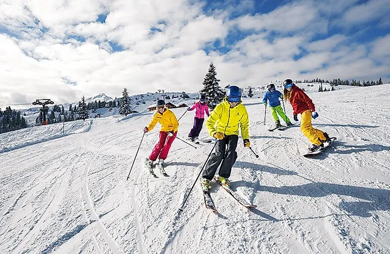 Skigruppe in bunter Winterkleidung fährt eine verschneite Piste in Flachau bei besten Wetterbedingungen hinunter.