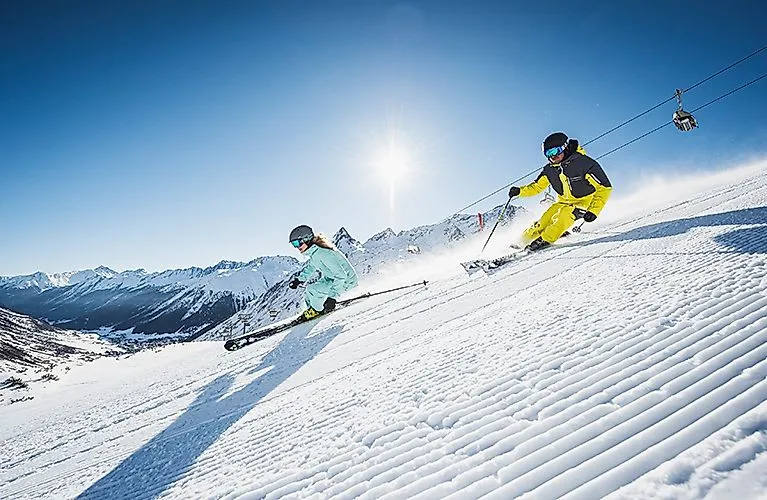 Zwei Skifahrer carven auf frisch präparierter Piste in Galtür unter strahlend blauem Himmel.