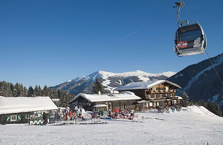 Winterlandschaft mit Gondelbahn und Skifahrern vor einer urigen Skihütte im Skigebiet Leogang-Saalbach in Österreich.