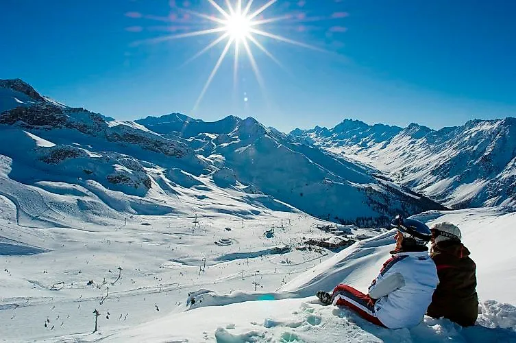 Two skiers enjoy the panorama of the snow-covered Silvretta Arena under the bright winter sun above Ischgl.