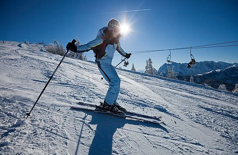Skifahrerin im Sonnenschein auf präparierter Piste im Skigebiet Kössen mit Sessellift und verschneitem Alpenpanorama im Hintergrund