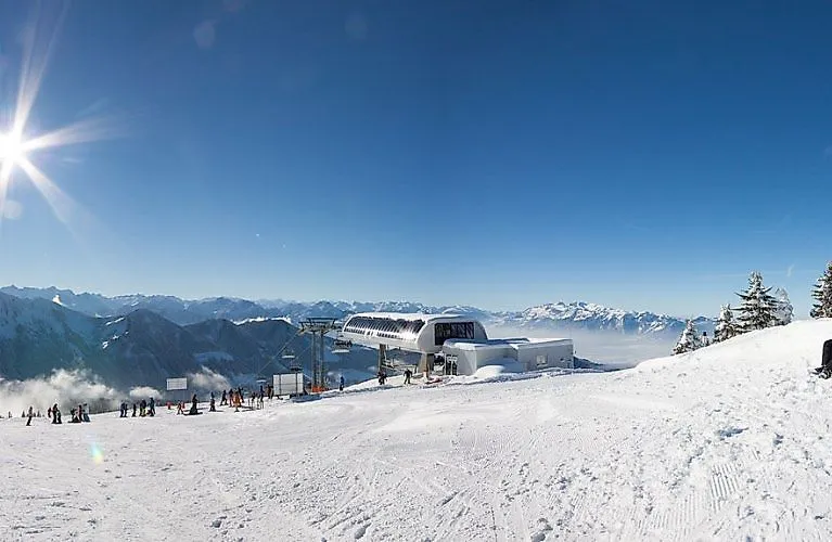 Skigebiet Laterns im Winter mit moderner Liftstation, Skifahrern und verschneiten Bergen unter strahlend blauem Himmel.