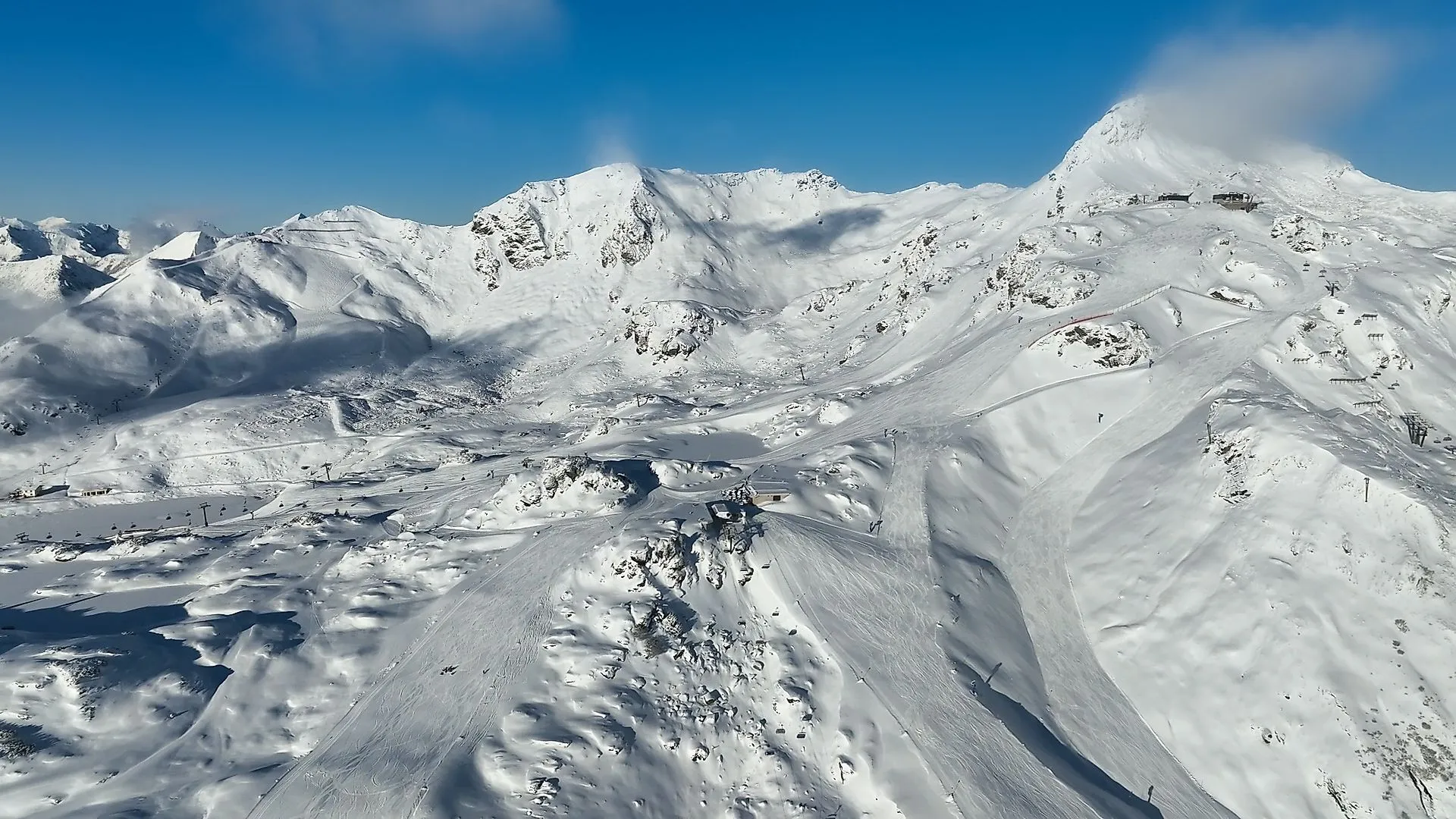 Aufnahme der FlyingCam von der verschneiten Berglandschaft und Pisten im Skigebiet Obertauern bei strahlend blauem Himmel.