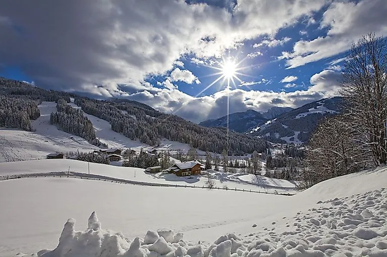 Schneebedeckte Winterlandschaft in Wagrain mit strahlendem Sonnenschein, Skipisten und urigen Almhütten im Hintergrund.