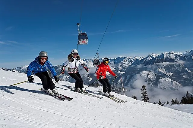 Drei Skifahrer fahren parallel auf einer Piste mit Blick auf die verschneiten Berge am Feuerkogel.