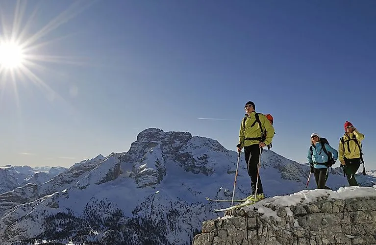 Tres esquiadores de travesía en Sesto con los Dolomitas nevados al fondo bajo el sol