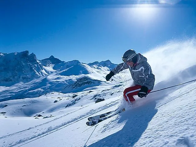 Skifahrer bei der Abfahrt auf einer verschneiten Piste in Savognin mit imposanter Alpenkulisse unter strahlend blauem Himmel.