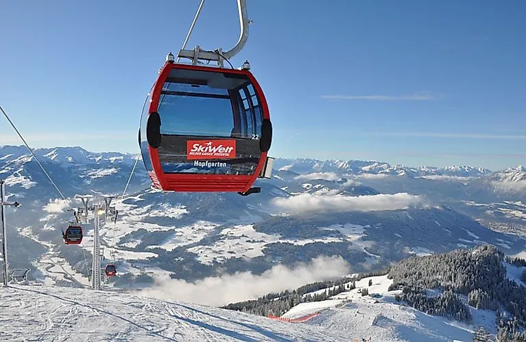 Rote Gondel der SkiWelt Wilder Kaiser-Brixental schwebt über die verschneite Winterlandschaft bei Scheffau in Tirol.