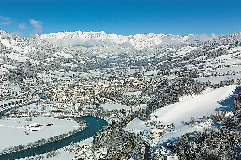 Verschneite Winterlandschaft mit Blick auf St. Johann im Pongau und die umliegenden Berge, unter einem klaren blauen Himmel.