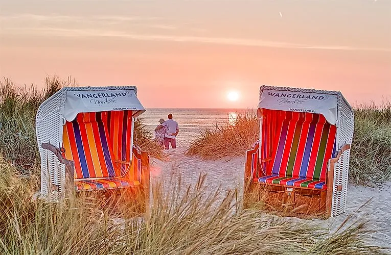 Zwei bunte Strandkörbe im Wangerland mit Blick auf Sonnenuntergang an der Nordsee, Paar spaziert am Strand