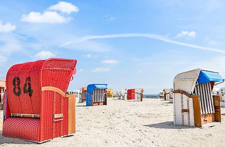 Bunte Strandkörbe am Sandstrand von Schillig an der Nordsee bei blauem Himmel