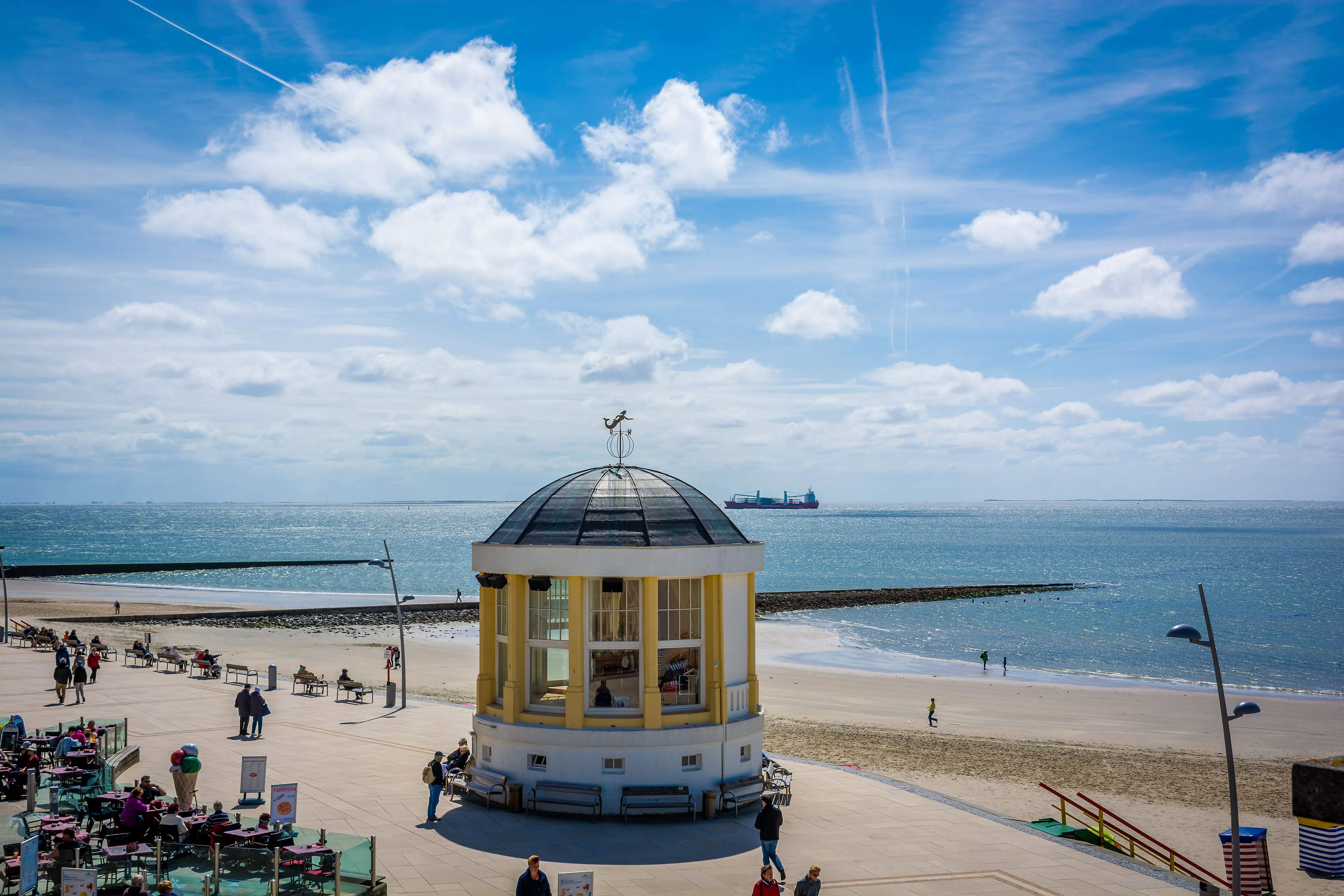Strandpromenade von Borkum mit Pavillon, Blick aufs Meer und Spaziergänger bei Sonnenschein.