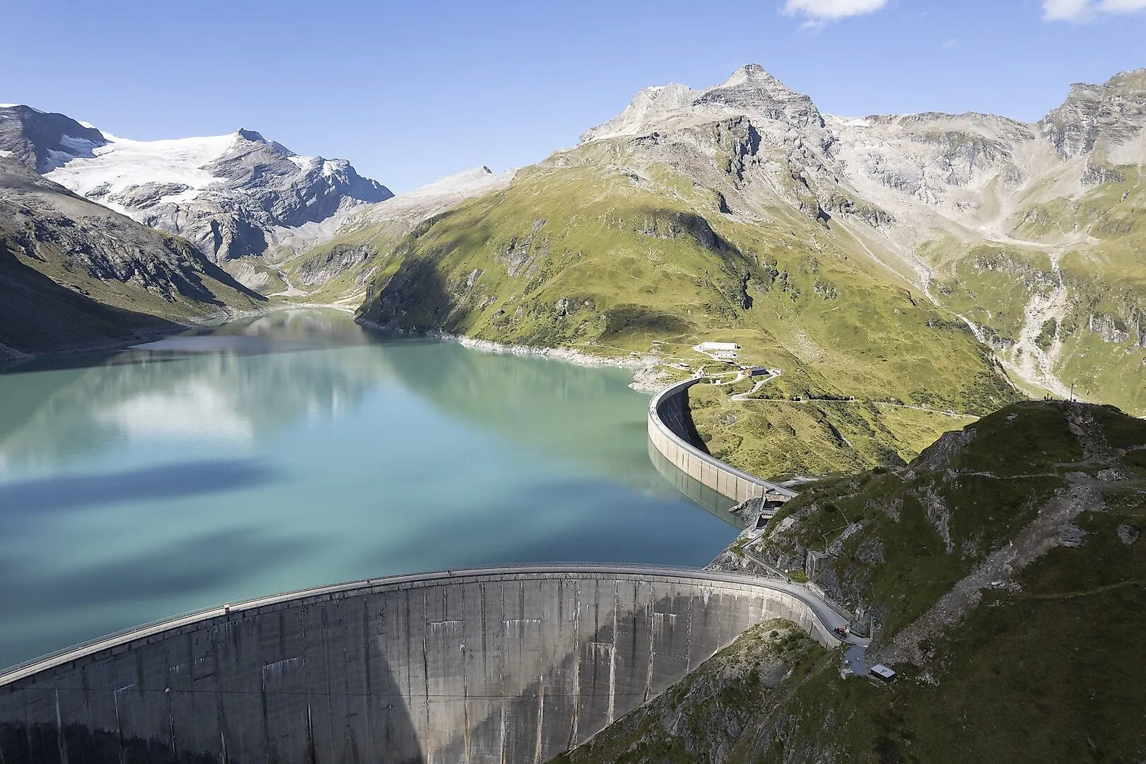Blick auf die Hochgebirgsstauseen Kaprun mit türkisblauem Wasser, umgeben von majestätischen Bergen und grünen Berghängen.