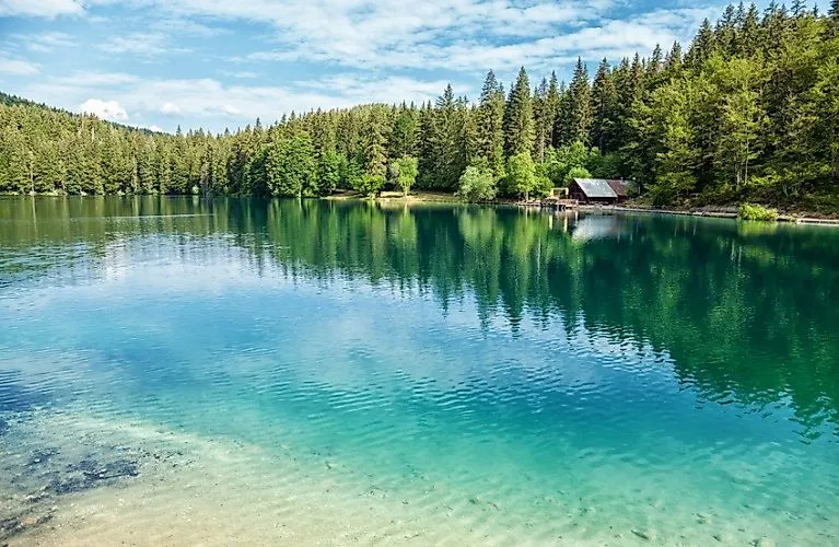 Il lago di Fusine, di colore turchese, a Tarvisio, circondato da boschi e montagne in un clima estivo limpido