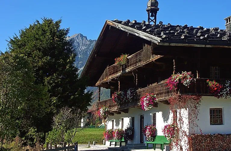 Traditionelles Tiroler Bauernhaus mit Blumenschmuck und Bergen im Hintergrund bei sonnigem Wetter.