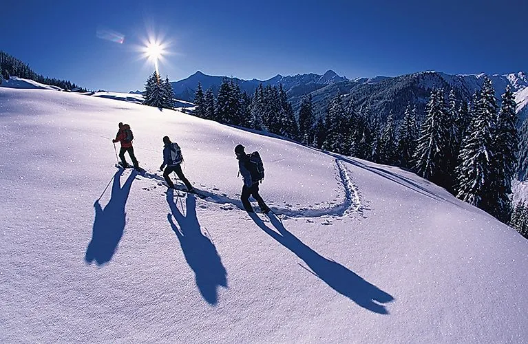 Drei Schneeschuhwanderer stapfen durch tief verschneite Winterlandschaft bei Uderns im Zillertal.