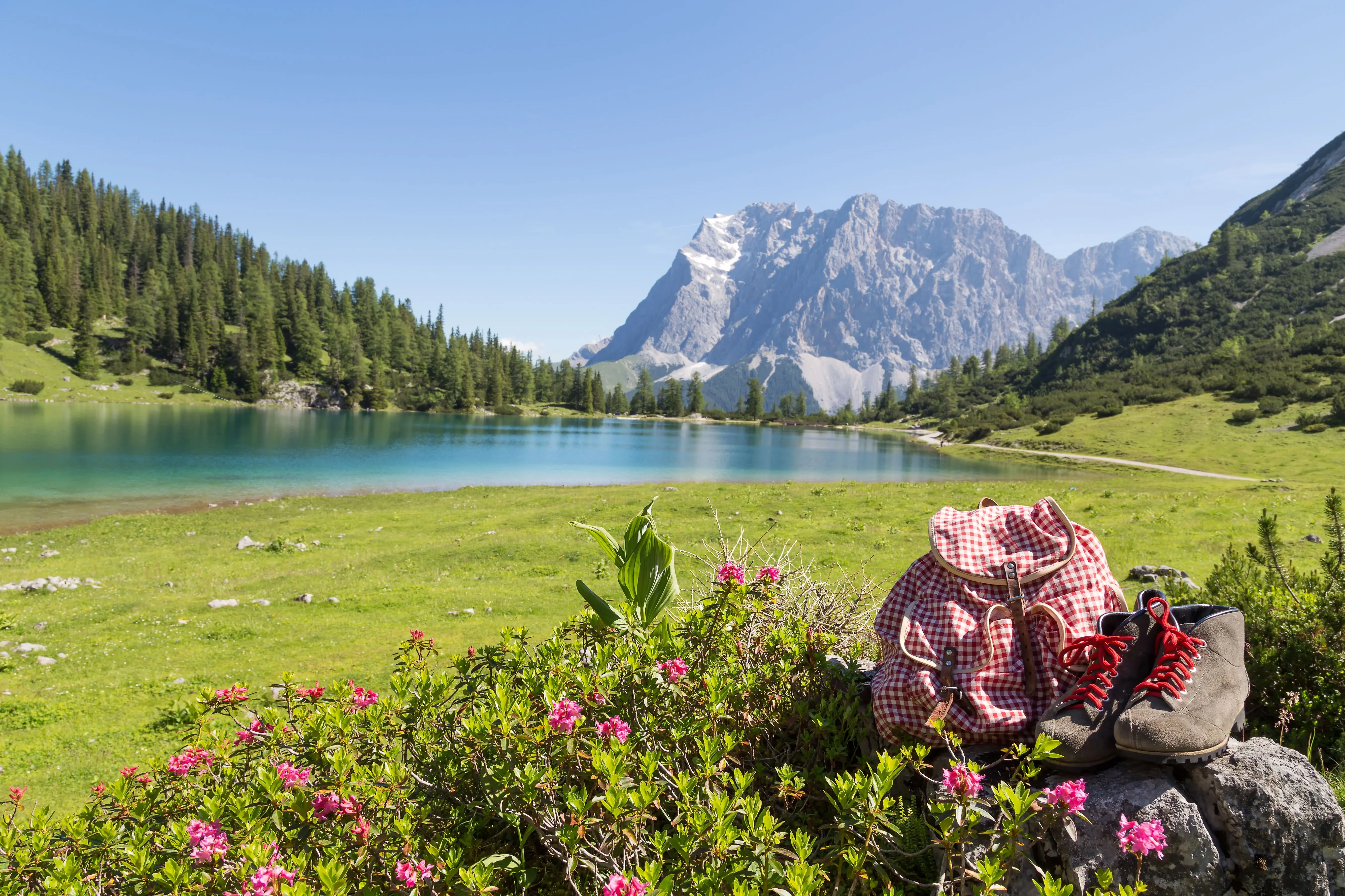 Idyllischer Bergsee unterhalb der Zugspitze mit Blumenwiese, Wanderrucksack und Bergschuhen im Vordergrund