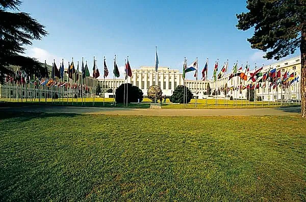 Sitz der Vereinten Nationen in Genf mit zahlreichen wehenden Nationalflaggen vor dem Gebäude
