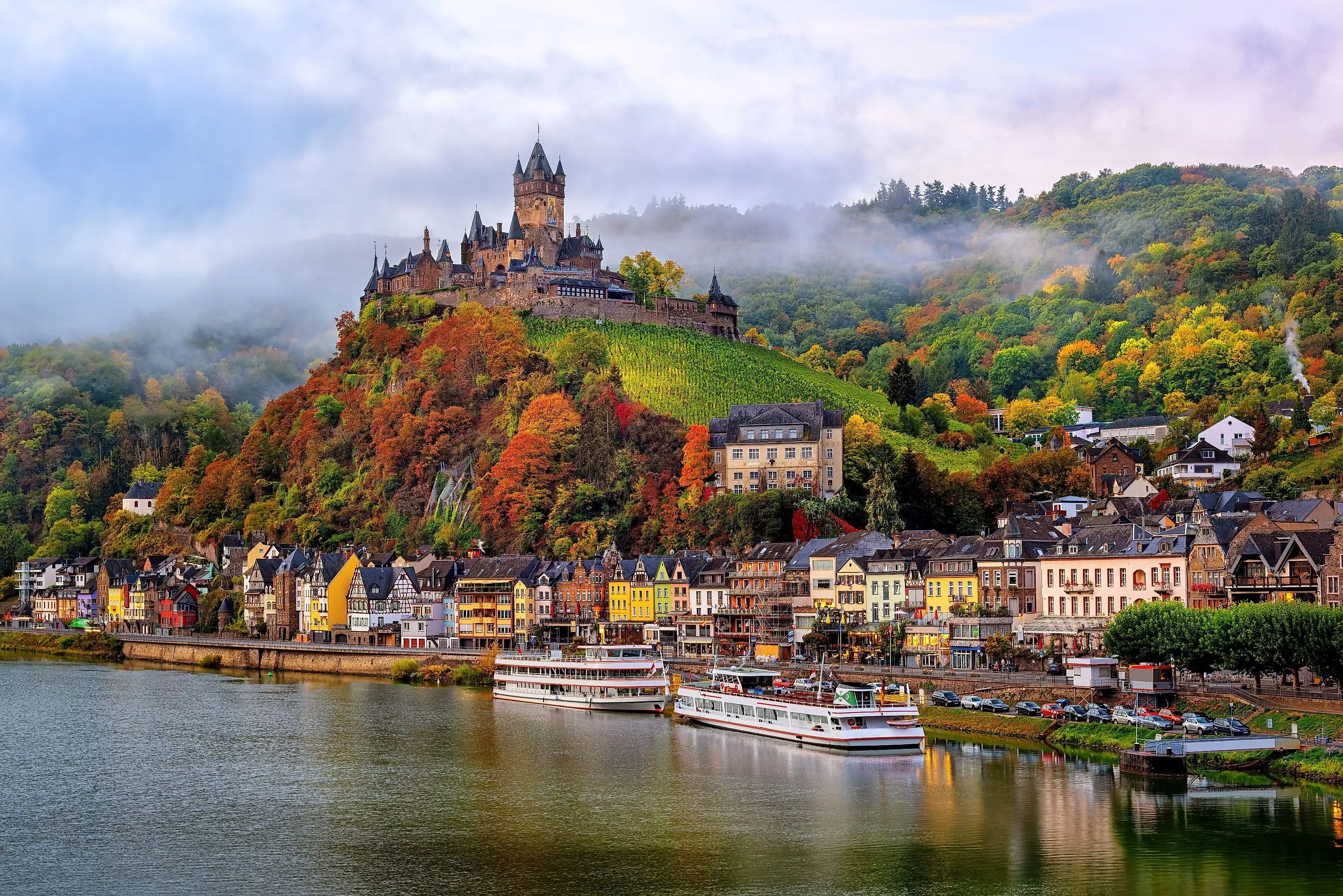 Reichsburg Cochem auf grünem Hügel über der Mosel mit bunten Häusern und Schiffen
