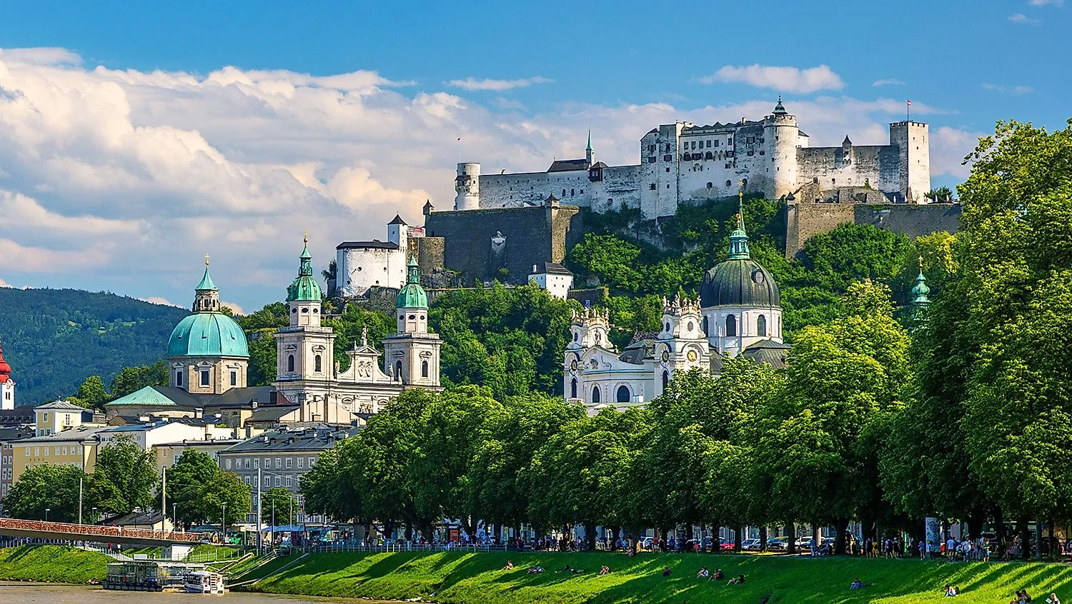 Panoramaaufnahme der Altstadt von Salzburg mit barocken Kirchenkuppeln und der imposanten Festung Hohensalzburg auf dem Hügel im Hintergrund.