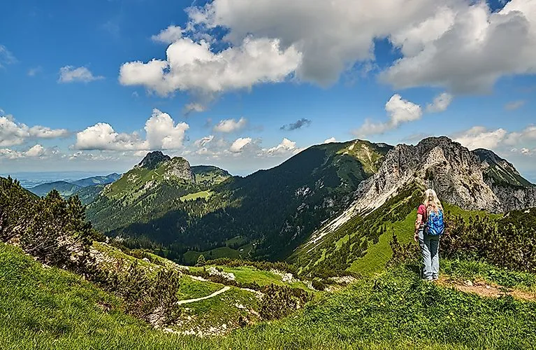 Wanderin mit Rucksack blickt auf das beeindruckende Alpenpanorama in Grän im Tannheimer Tal an einem sonnigen Tag.