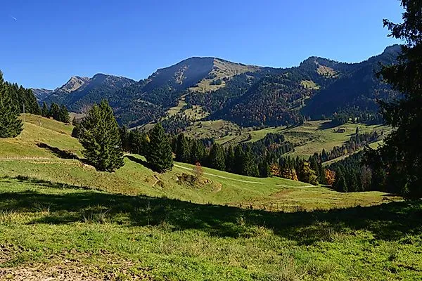 Blick auf die Nagelfluhkette bei Oberstaufen mit sanften Wiesen und Wäldern an einem sonnigen Herbsttag.