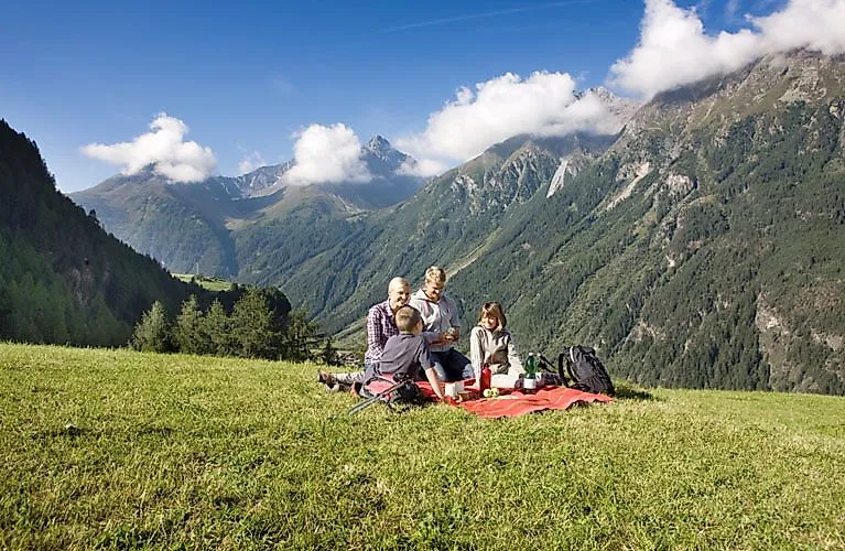 Familie macht ein Picknick auf grüner Wiese in den Bergen bei Oetz im Ötztal an einem sonnigen Wandertag.