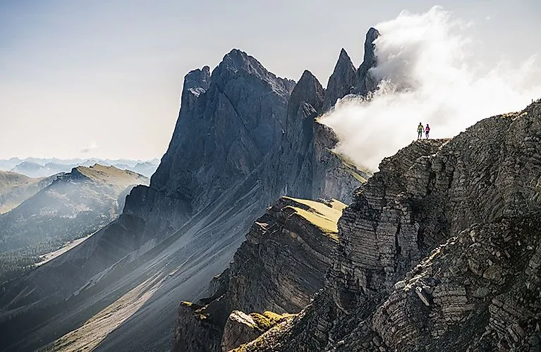 Twee wandelaars op een steile Dolomietenkam omgeven door wolken en rotsen