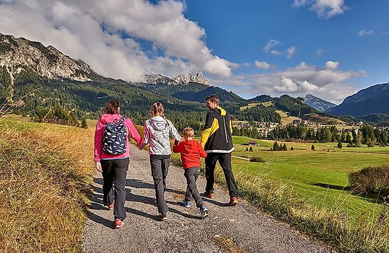Familie beim Wandern auf einem idyllischen Weg im Tannheimer Tal mit Blick auf das Dorf Grän und die umliegenden Berge.