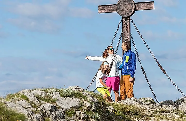 Familienwanderung am Hochkar: Drei Personen am Gipfelkreuz mit Blick auf die Alpen bei Göstling