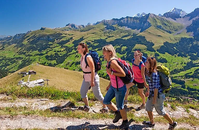 Wandergruppe auf sonnigem Bergpfad mit Aussicht auf das grüne Tal bei Adelboden in der Schweiz
