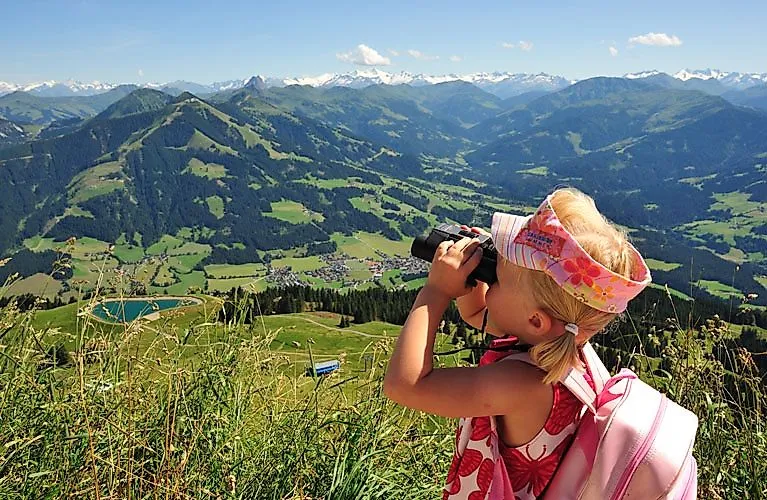 Mädchen mit Fernglas genießt den Panoramablick auf die Tiroler Bergwelt beim Wandern oberhalb von Hopfgarten in der SkiWelt Wilder Kaiser.