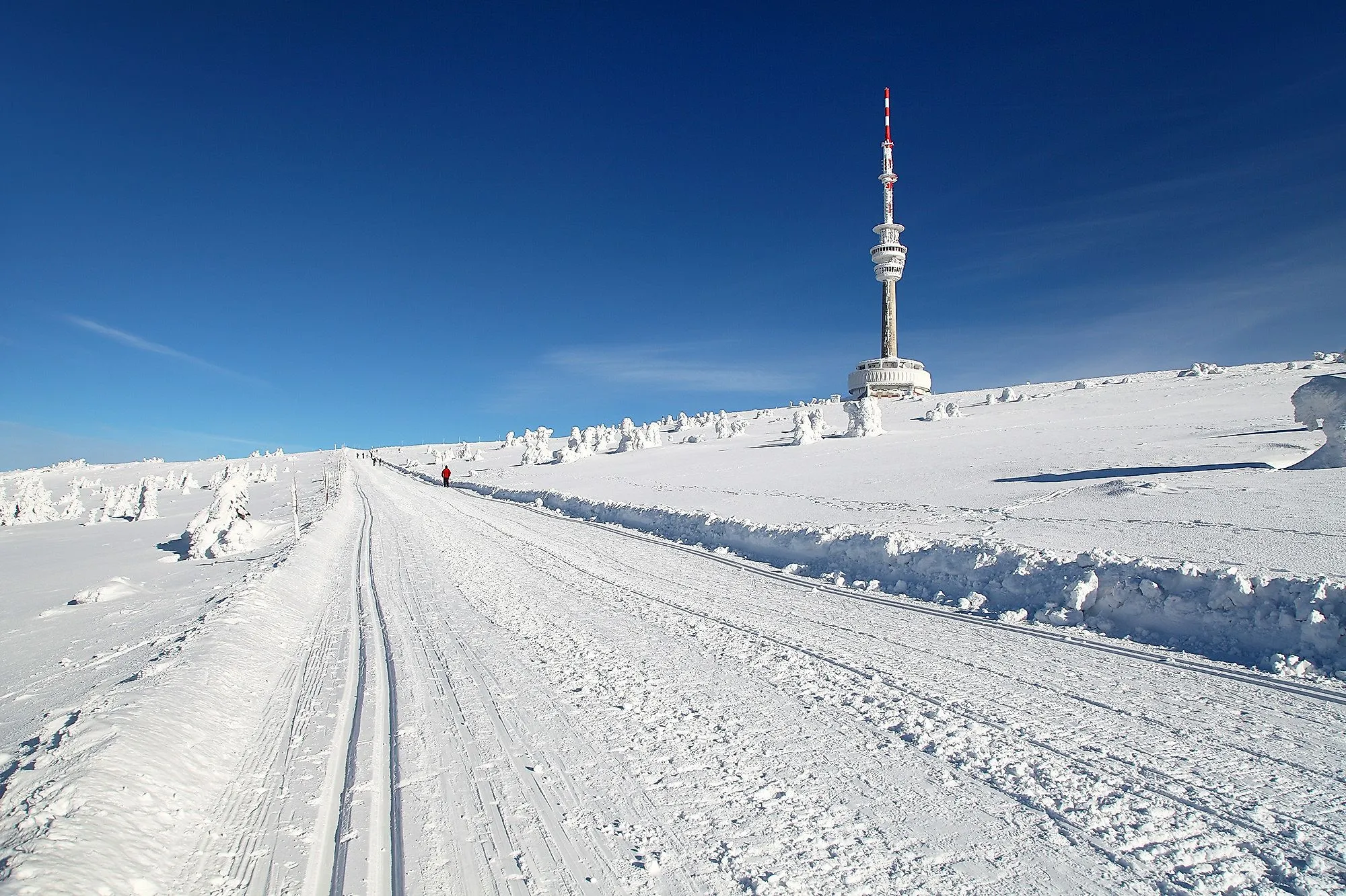 Winterlandschaft am Praděd mit Loipe, Schneefiguren und Aussichtsturm unter blauem Himmel.
