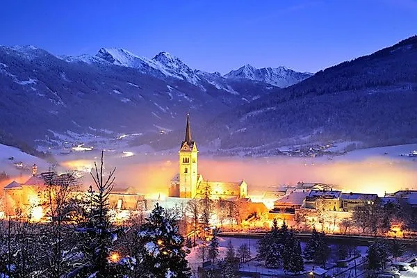 Winterliche Stadtansicht von Radstadt mit leuchtender Kirche und verschneiten Bergen.