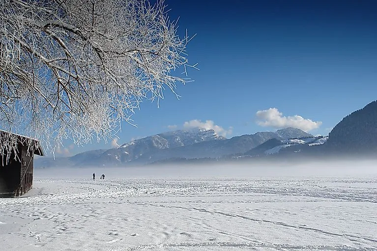 Winterlandschaft am Walchsee mit schneebedecktem Feld und Alpen im Hintergrund bei klarem Himmel