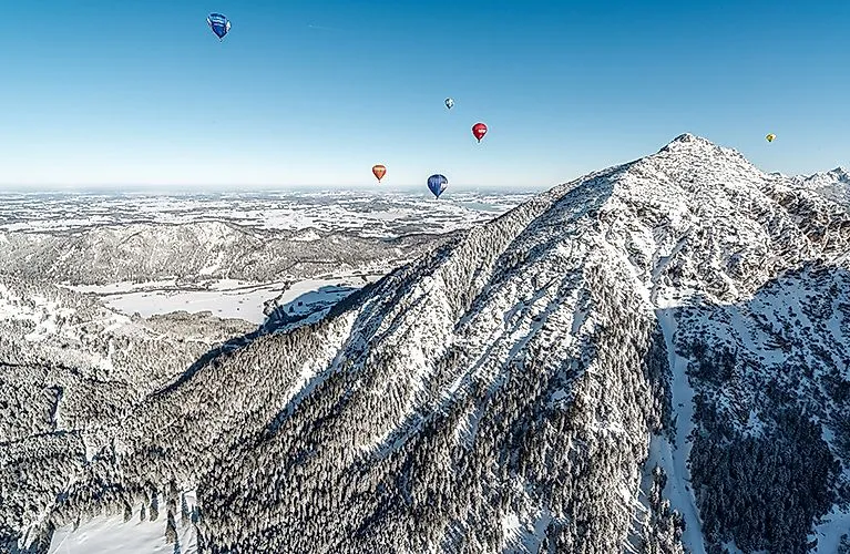 Schneebedeckte Berglandschaft im Tannheimer Tal mit bunten Heißluftballons am Himmel bei Grän im Winter.